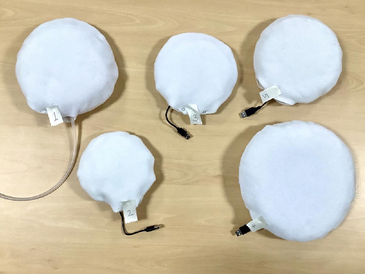 Photo of the five final calming cushion prototypes, all circular with white soft fabric covers.