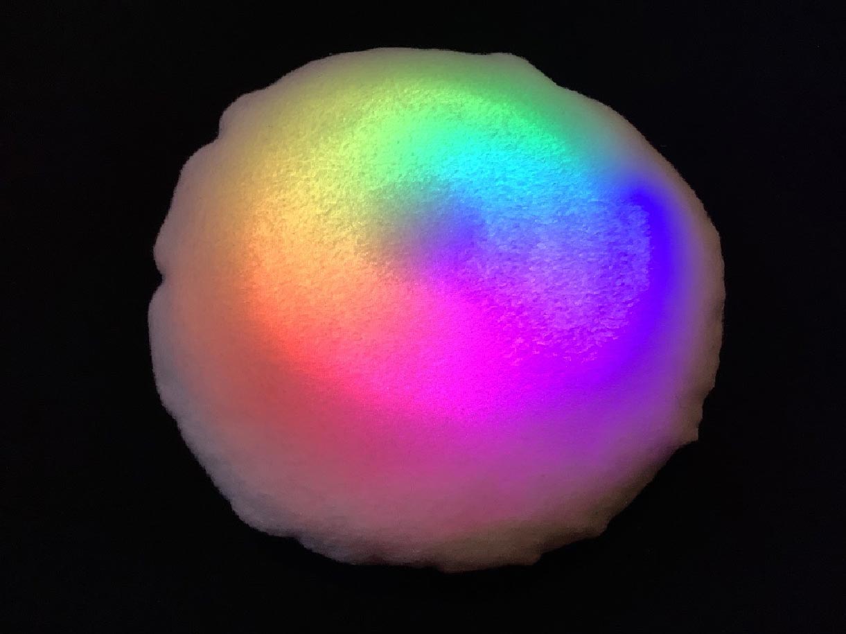 Photo of one of the cushion prototypes, a round cushion with a circular rainbow of coloured light shining through the fabric cover.